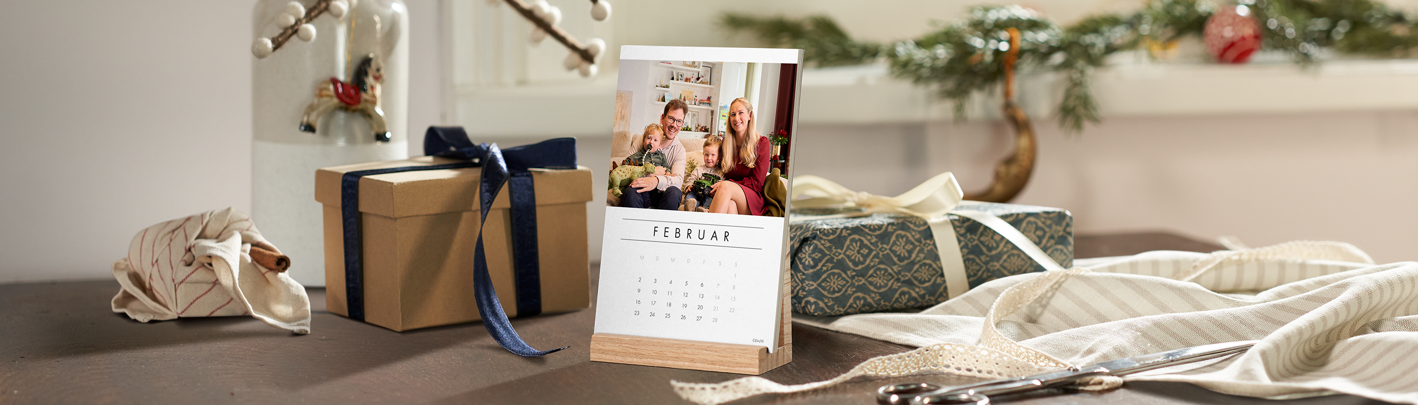 Ein Fotokalender aus einzelnen Kalenderblättern auf einem Holzaufsteller mit dem Monat Februar und dem Foto einer jungen Familie.