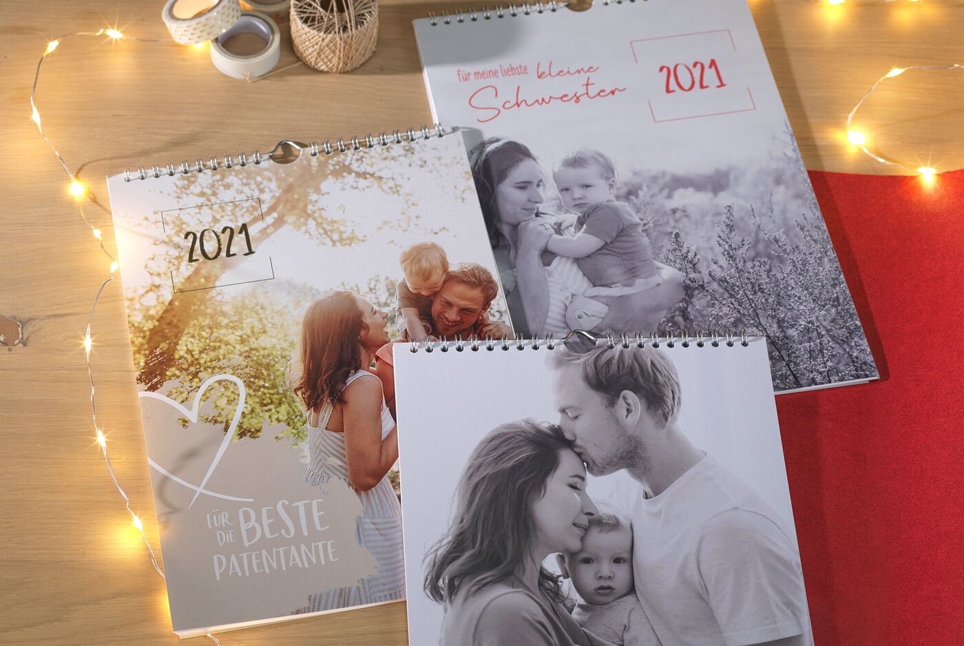Drei CEWE Fotokalender 2021 auf einem Tisch, umgeben von lichterketten.