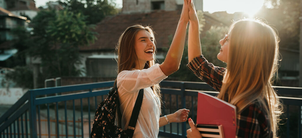 Zwei fröhliche Personen geben sich ein High-Five in der Abendsonne.