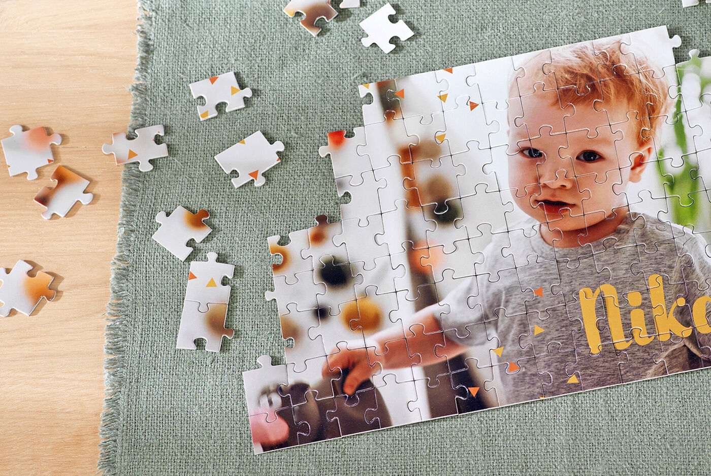 Ein nahezu fertiges Foto-Puzzle mit bunten Teilen, gelegt auf einem grünen Tuch. Es zeigt einen Teil des Bildes eines kleinen Kindes, das glücklich spielt.
