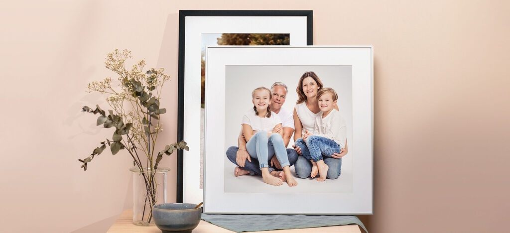 Familie posiert glücklich in einem Rahmen, im Hintergrund ein Pflanzenarrangement.