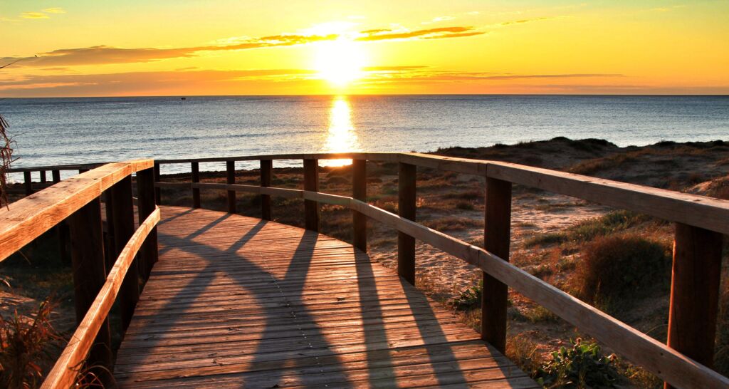 Holzsteg am Meer bei Sonnenuntergang mit langen Schatten auf den Planken