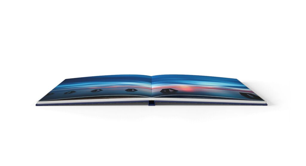 Aufgeschlagenes CEWE FOTOBUCH mit Fotopapier und Lay-Flat-Bindung. Auf den Seiten ist eine Aufnahme eines Sonnenuntergangs.