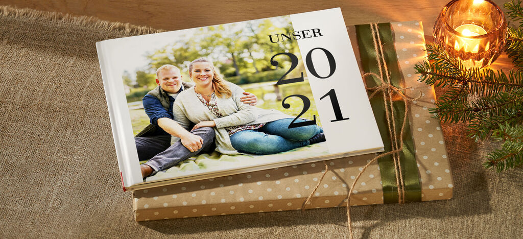 Ein schön gestaltetes CEWE FOTOBUCH liegt zusammen mit Geschenken auf einem Tisch. Es zeigt Erinnerungen aus dem Jahr 2021.