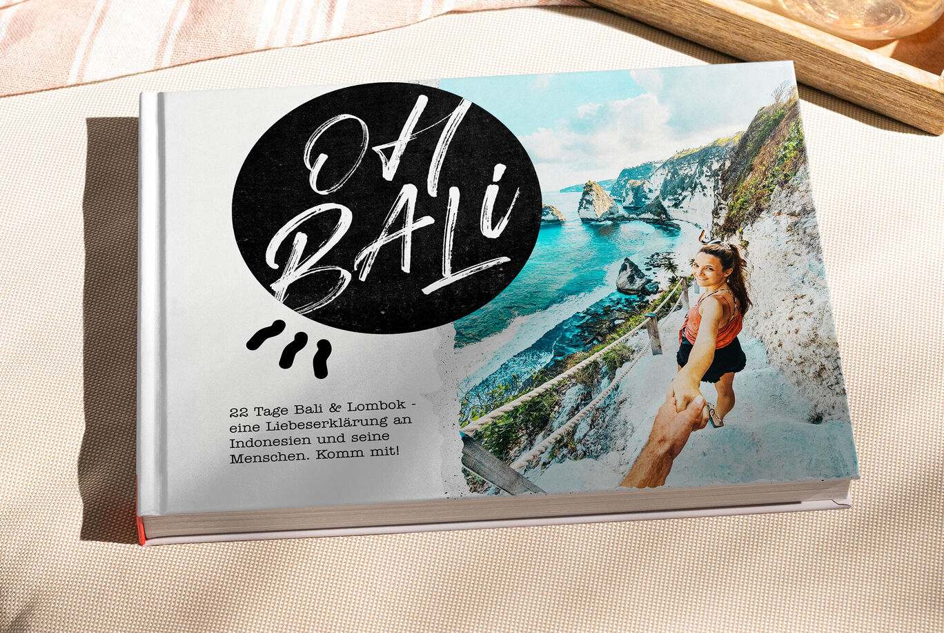 Ein kreatives Fotobuch mit dem Titel "Oh Bali" auf einem Tisch, umgeben von Natur. Eine Frau läuft lächelnd auf einem Weg, der zur Küste führt.