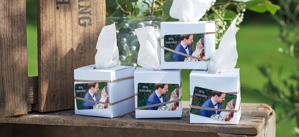 Vier hübsch verpackte Geschenke mit weißem Papier und dekorativem Band stehen auf einem Holztisch. Jedes Geschenk zeigt ein romantisches Foto eines Paares.