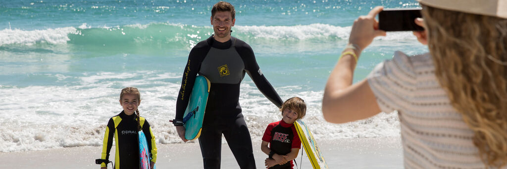 Familie am Strand mit Surfbrettern, Mutter macht Foto