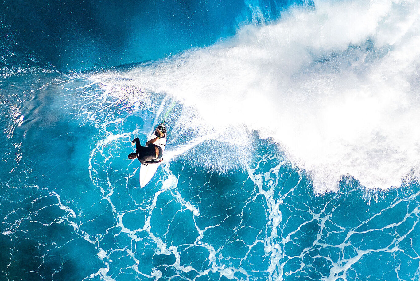 Ein Surfer reitet auf einer riesigen Welle im glitzernden blauen Ozean. Es ist ein wunderschöner Moment im Wasser.