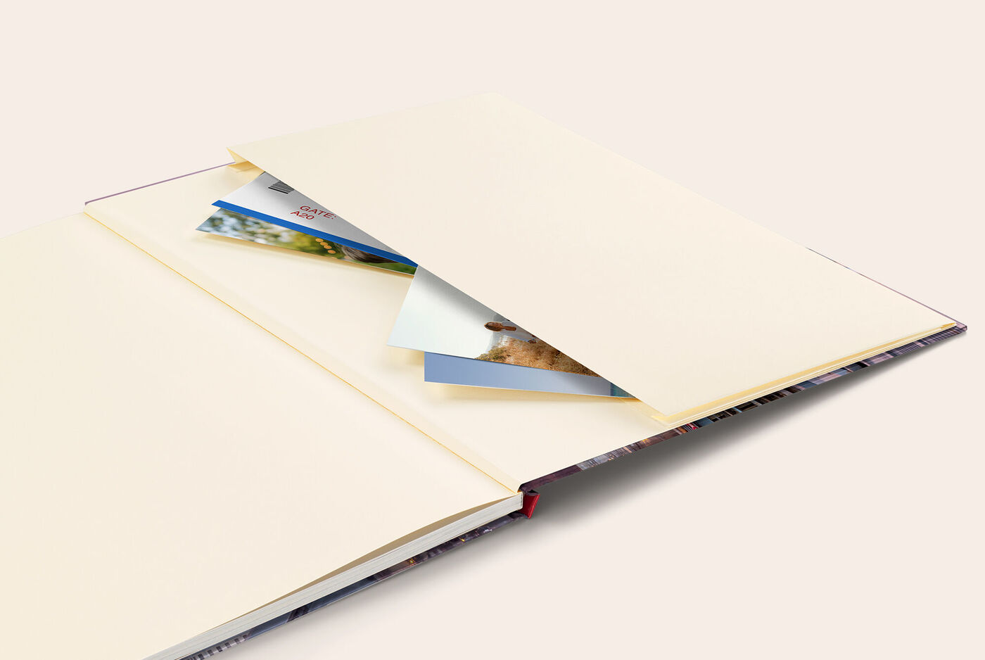 Ein geöffnetes CEWE FOTOBUCH mit Erinnerungstasche im Einband. Die Tasche ist gefüllt mit Fotoabzügen.