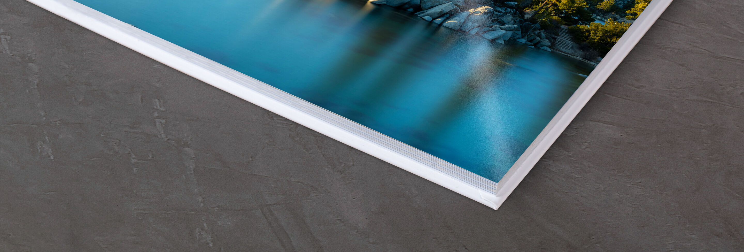 Ecke eines professionellen Fotobuchs, das auf einem Tisch liegt, mit Wasser und Bäumen im Hintergrund