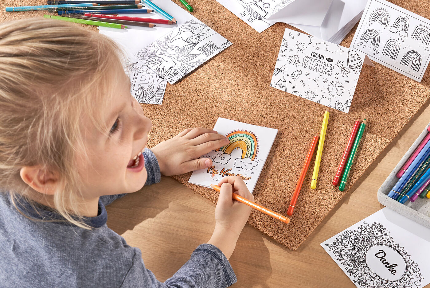 Ein Kind malt mit Buntstiften auf einem Tisch und ergänzen eine selbst gestaltete Grußkarte.