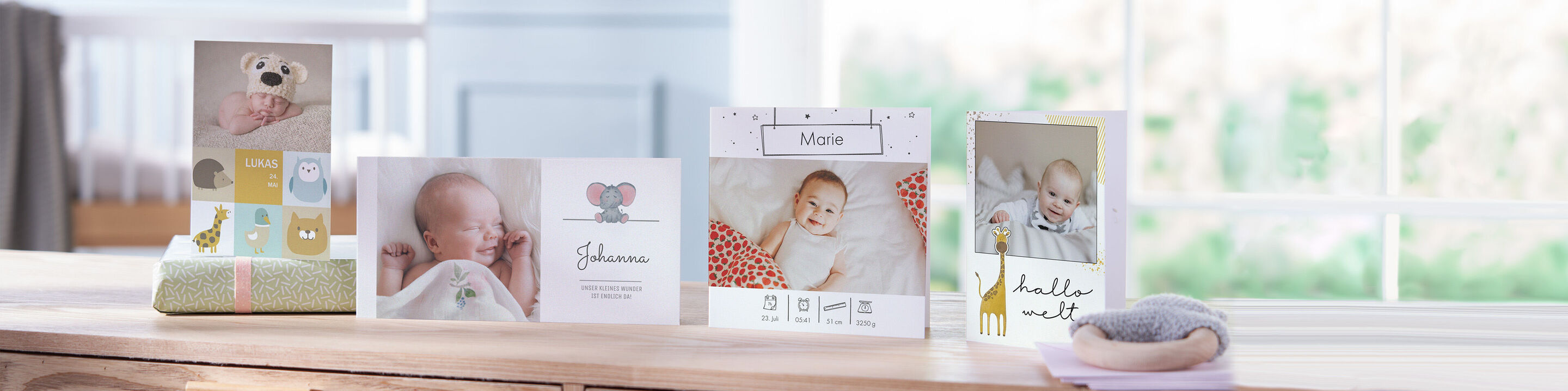 Verschiedene CEWE Grußkarten und ein CEWE FOTOBUCH mit Babyfotos stehen auf einem Holztisch.