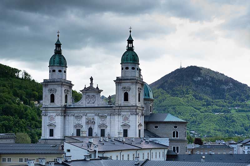 Die barocke Kirche mit zwei Türmen und grünem Dach vor einer bewaldeten Berglandschaft
