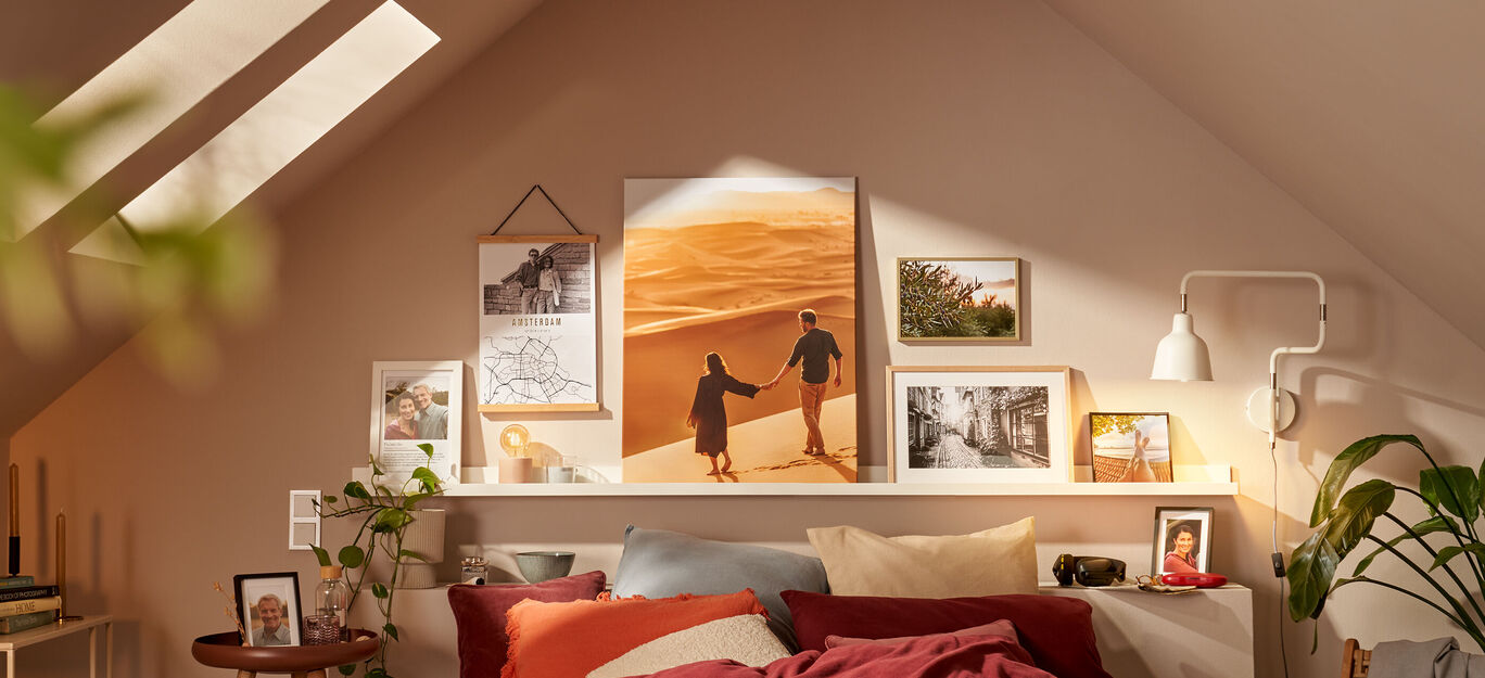Ein gemütlich eingerichtetes Schlafzimmer mit warmen Farben. An der Wand hängen Bilder von einem Paar in den Dünen. Der Raum strahlt Lebensfreude aus.