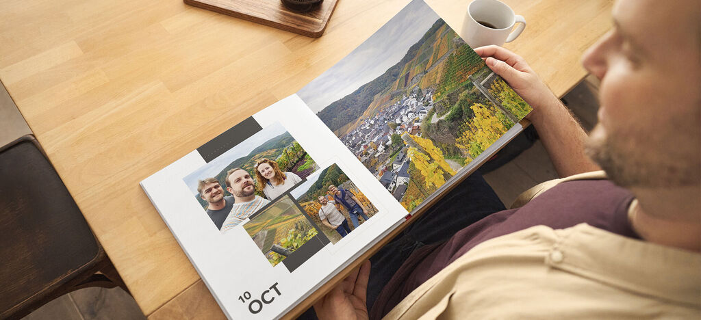 Eine Person blättert durch ein CEWE FOTOBUCH mit Fotos von einem Ausblick auf eine grüne Landschaft und mehreren Personen.