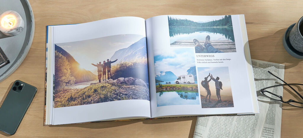 Ein offenes CEWE FOTOBUCH liegt auf einem Holztisch. Es zeigt wunderschöne Erinnerungen an einen Urlaub in der Natur.
