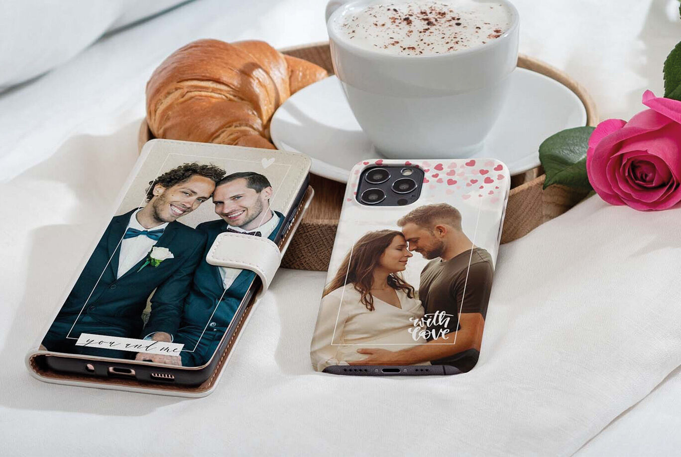 Zwei personalisierte Handyhüllen auf einem Tisch mit einem Croissant und einer Tasse Kaffee. Die Hüllen zeigen emotionale Fotos von Paaren.