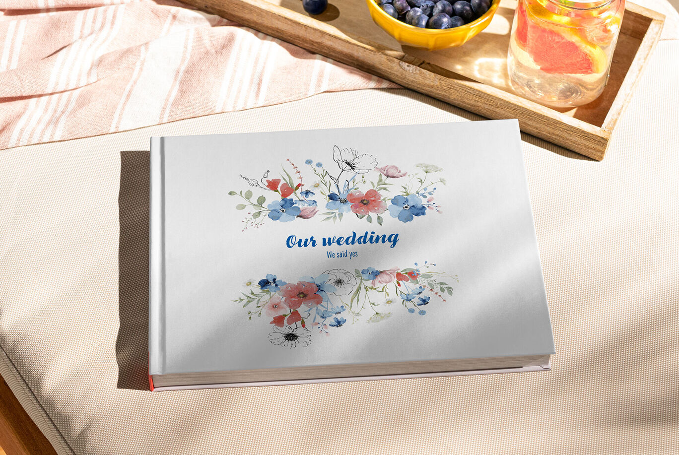 Ein CEWE Fotobuch mit Blumenmuster und dem Titel "Our wedding" liegt auf einem Tisch.