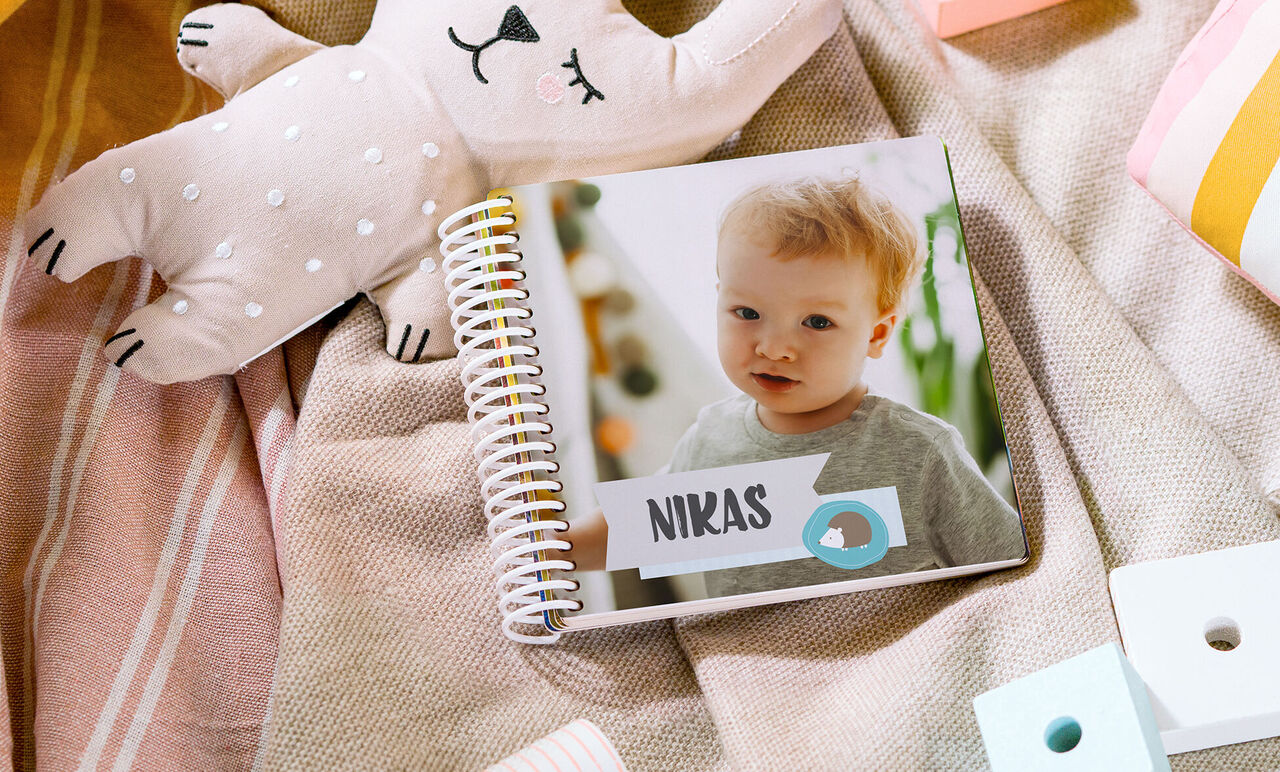 Ein liebevoll gestaltetes Fotobuch mit dem Namen Nikas auf dem Cover, umgeben von gemütlichen Textilien und einem Stofftier.