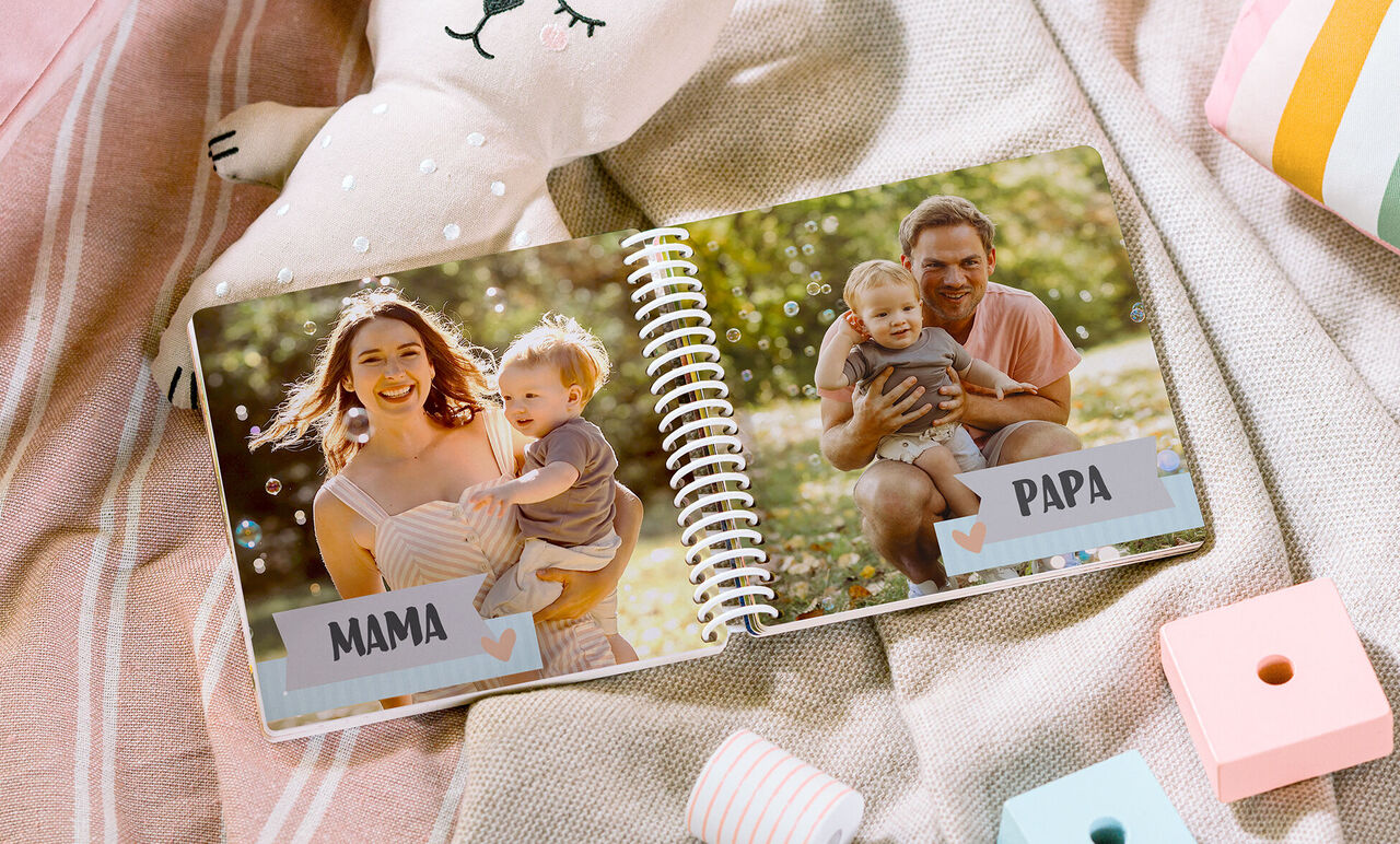 Ein offenes CEWE FOTOBUCH mit Familienfotos im Freien. Links eine Mutter mit einem Kind, rechts ein Vater mit einem Kind.