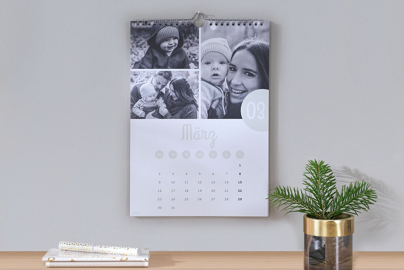 Ein dekorativer Wandkalender mit ansprechenden schwarz-weiß-Fotos von glücklichen Momenten. Der Kalender zeigt den Monat März und ist zusammen mit einer grünen Pflanze auf einem Tisch platziert