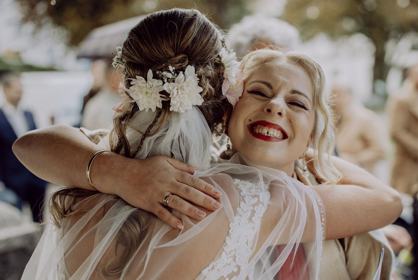 Zwei Frauen umarmen sich liebevoll nach einer Hochzeit, eine trägt ein Brautkleid und Blumen im Haar