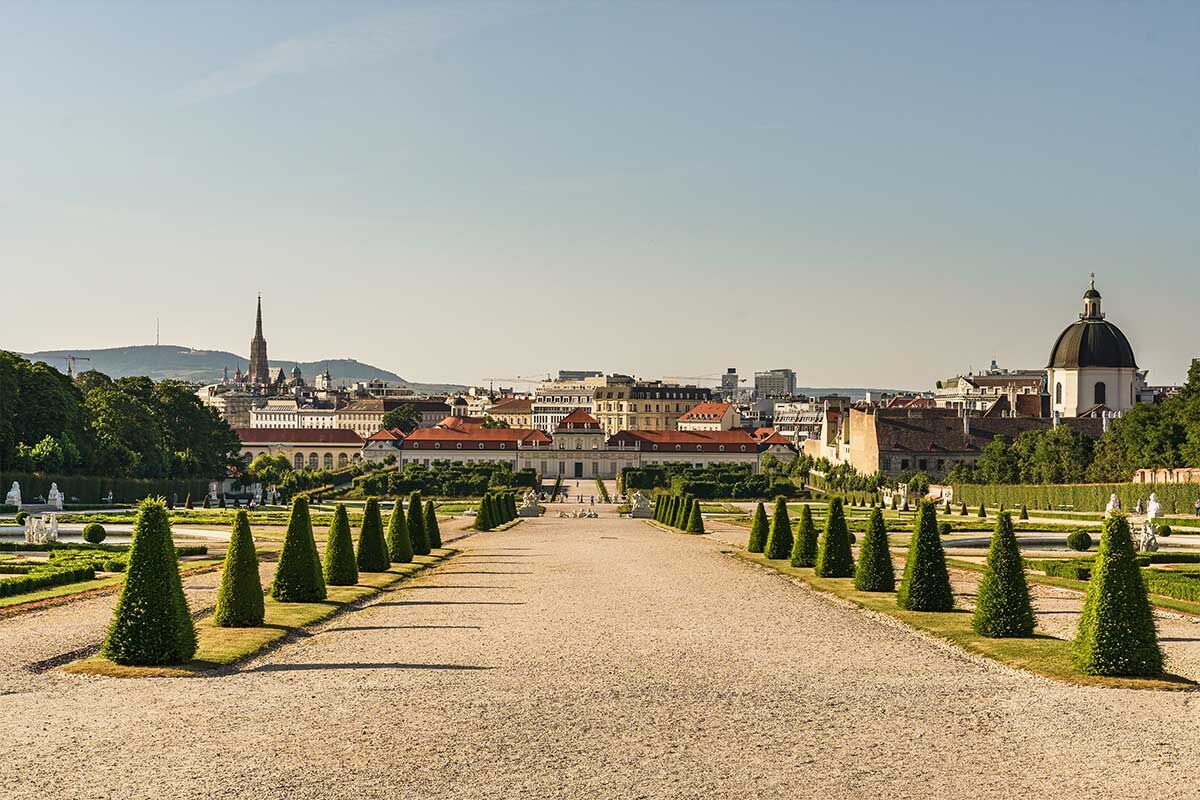 Blick auf den Schlossgarten von Schönbrunn mit grünen, schmalen Tannenbäumen und einer klaren blauen Himmel. Ein friedlicher Ort für Erinnerungen.