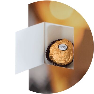 Eine goldene Praline in einer offenen Schachtel mit buntem Hintergrund