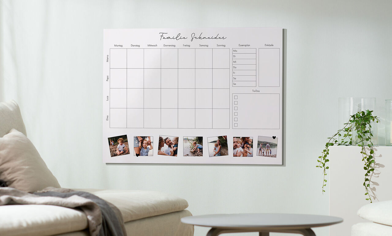 Ein Wandkalender mit Bildern von glücklichen Familienmomenten und einem klaren Design auf einem hellen Wand im Wohnzimmer