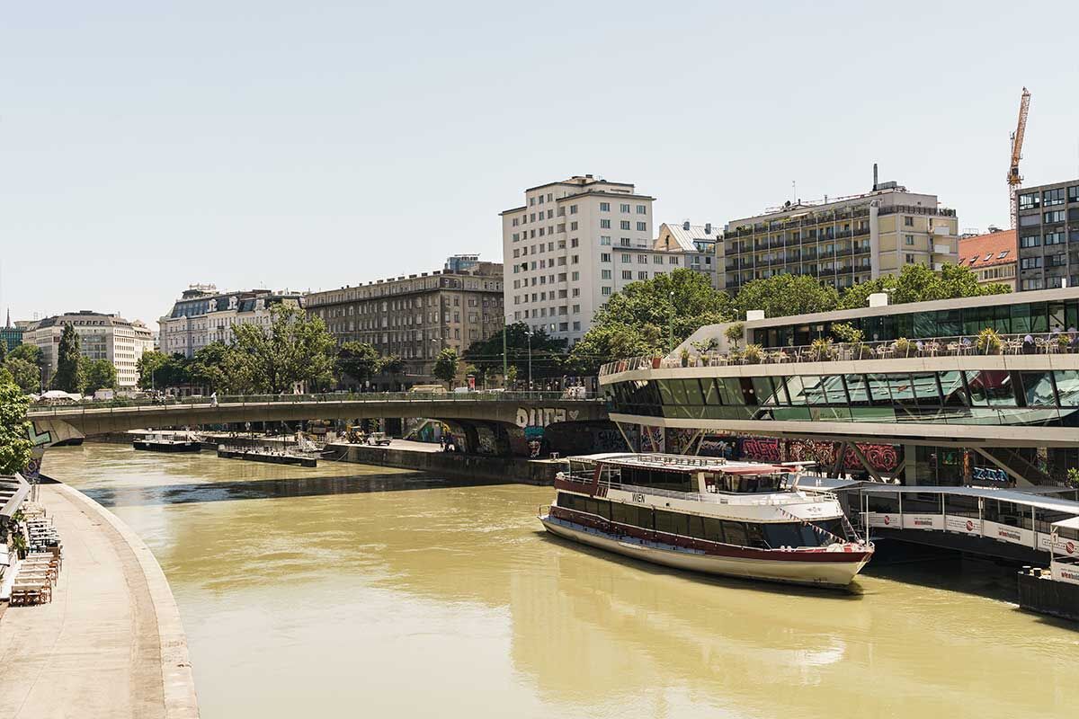 Ufer des Flusses mit modernen Gebäuden und einem Boot in Wien.