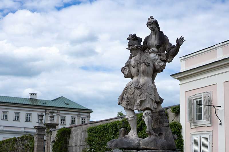 Eine beeindruckende Statue eines Paares vor einem großen historischen Gebäude mit grüner Umrandung.