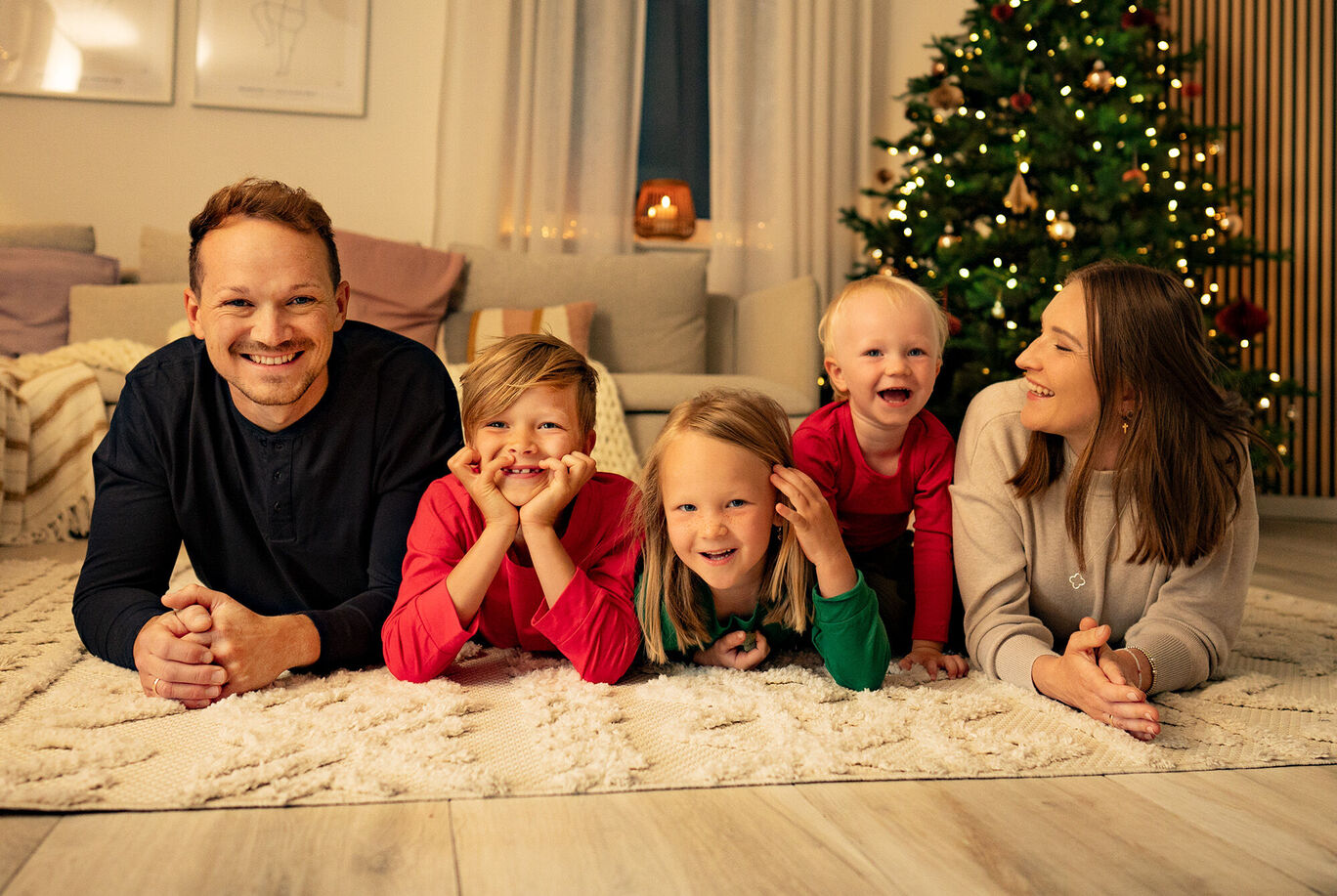 Familie liegt gemütlich auf dem Boden und genießt die Zeit zusammen vor einem festlich geschmückten Tannenbaum