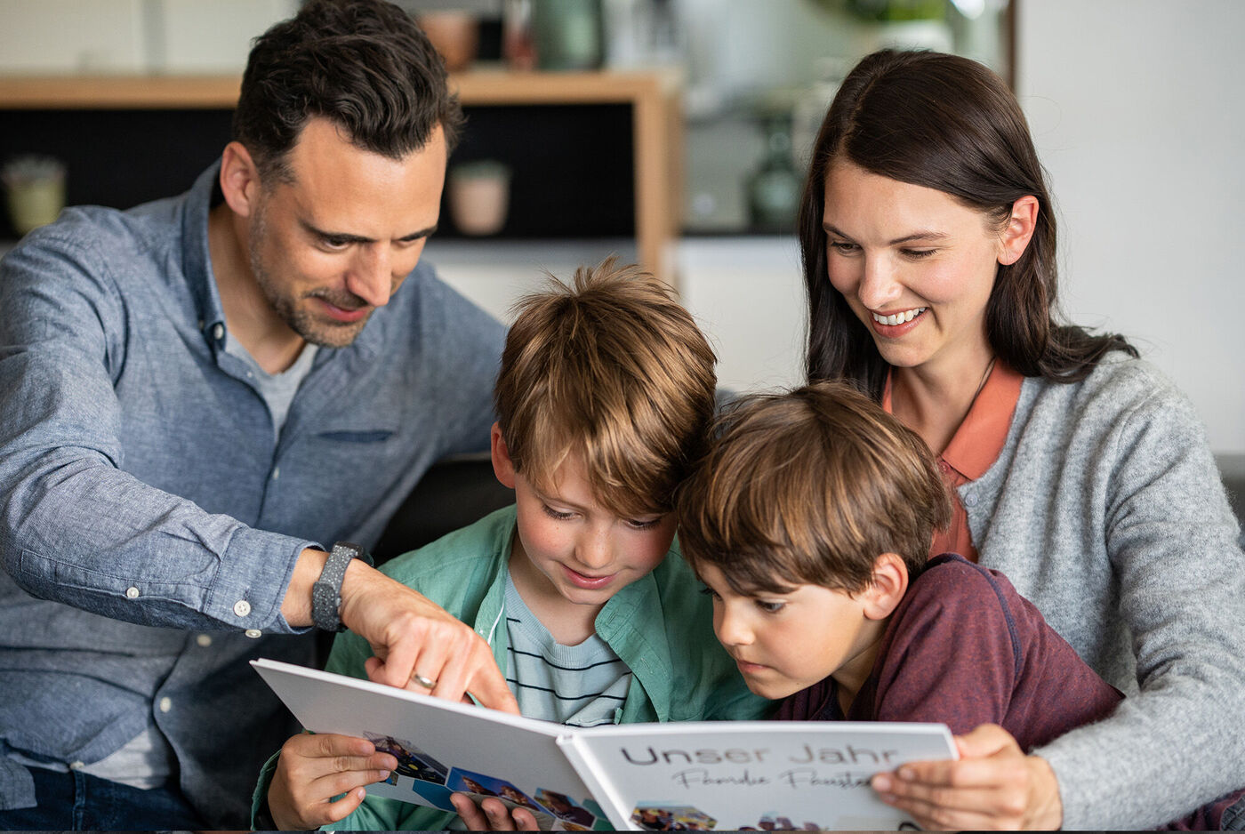 Eine Familie betrachtet gemeinsam ein CEWE FOTOBUCH mit dem Titel 'Unser Jahr'.