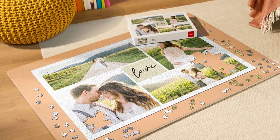Premium-Fotopuzzle von CEWE mit Bildern eines Paares in einer Weinlandschaft, umgeben von verstreuten Puzzleteilen und Blumen im Vordergrund