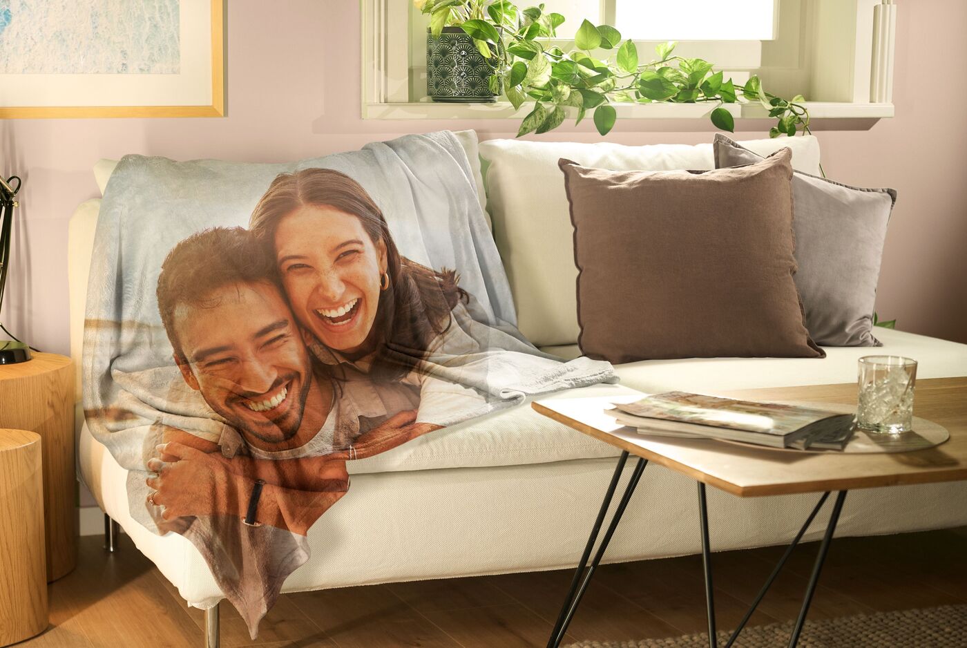 Eine bequeme Couch mit einer bunten Decke, auf der ein schnappschuss ist. Der Raum ist hell und freundlich mit Pflanzen im Hintergrund.