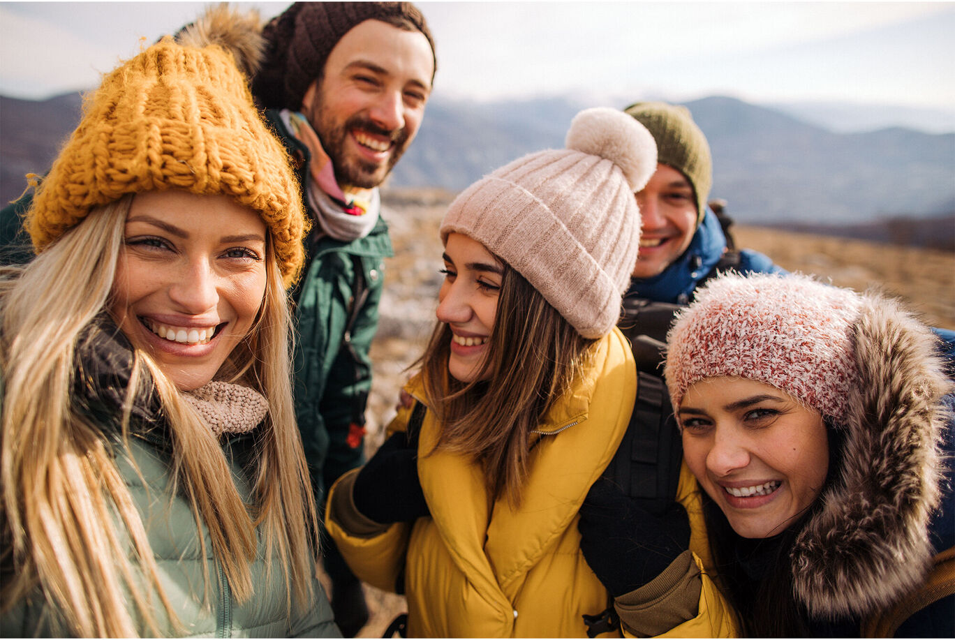 Gruppenschnappschuss von Freunden in warmen Winterjacken, mit bunten Mützen und Schals, die gemeinsam die Natur genießen.