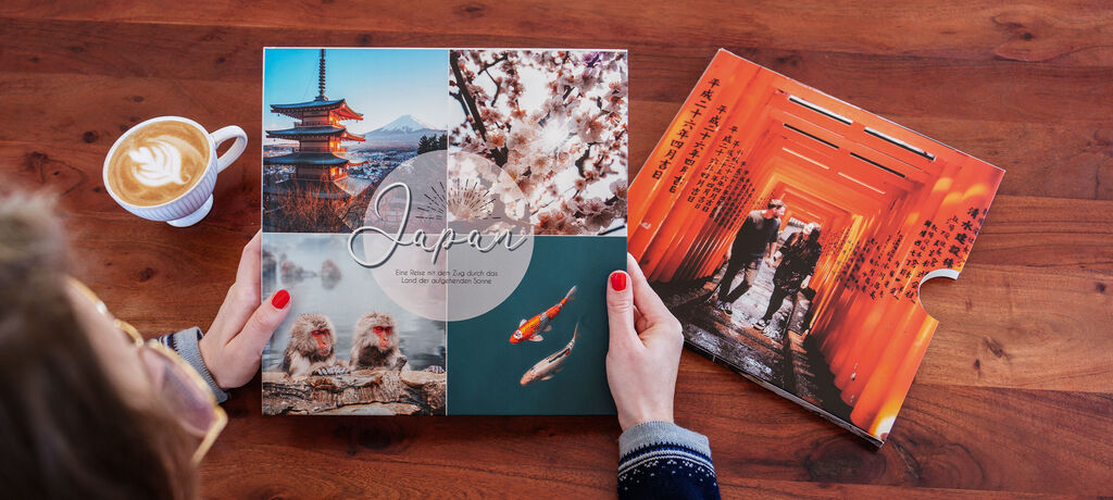 Eine Person hält ein CEWE Fotobuch mit einem Cover über Japan. Eine Tasse Kaffee liegt daneben. Der Tisch ist aus Holz mit einer warmen Auss