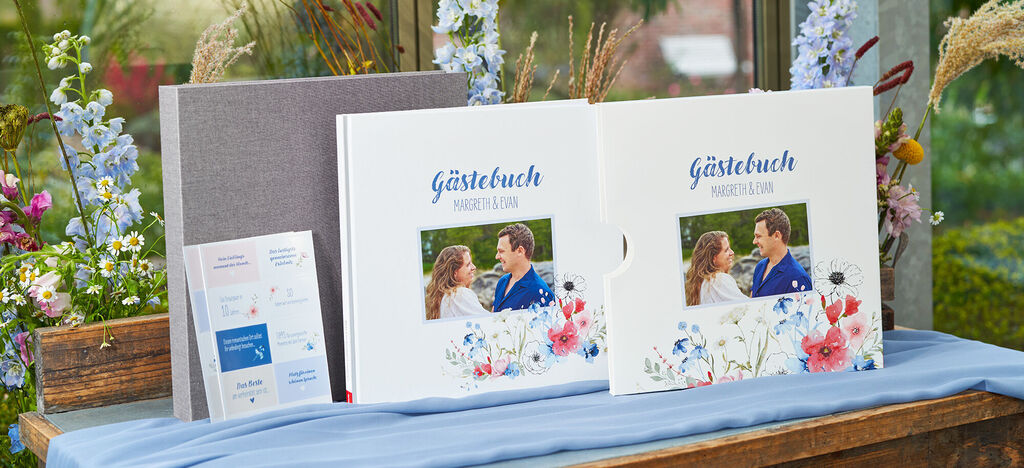Zwei freundliche Paare betrachten gemeinsam ein CEWE FOTOBUCH auf einem Holztisch umgeben von Blumen.