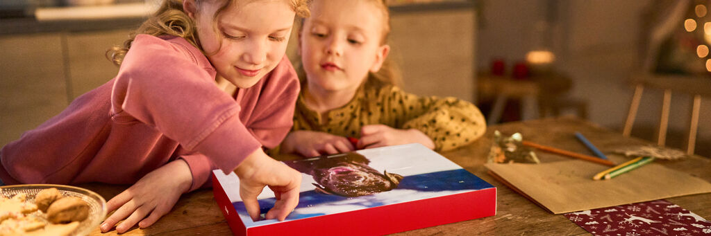 Zwei Kinder zeigen mit dem Finger auf ein CEWE FOTOBUCH mit einem Hundebild.