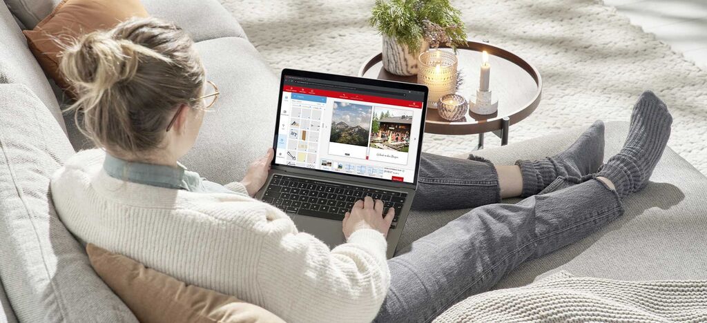 Frau sitzt auf der Couch und gestaltet ein CEWE FOTOBUCH am Laptop