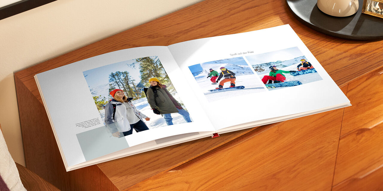 Ein offenes Fotobuch mit Erinnerungen an einen Winterurlaub. Links stehen zwei Personen im Schnee, rechts sind zwei Personen beim Snowboarden