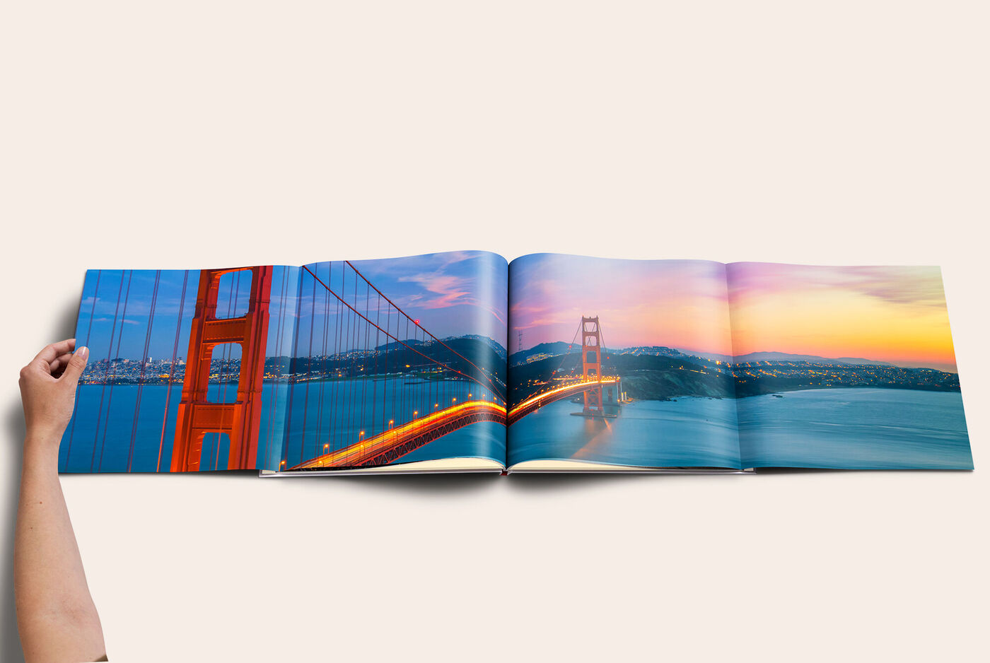 Von einer Hand geöffnetes CEWE FOTOBUCH mit Panoramaseite. Auf der Panoramaseite ist ein Bild der Golden Gate Bridge bei Sonnenuntergang.
