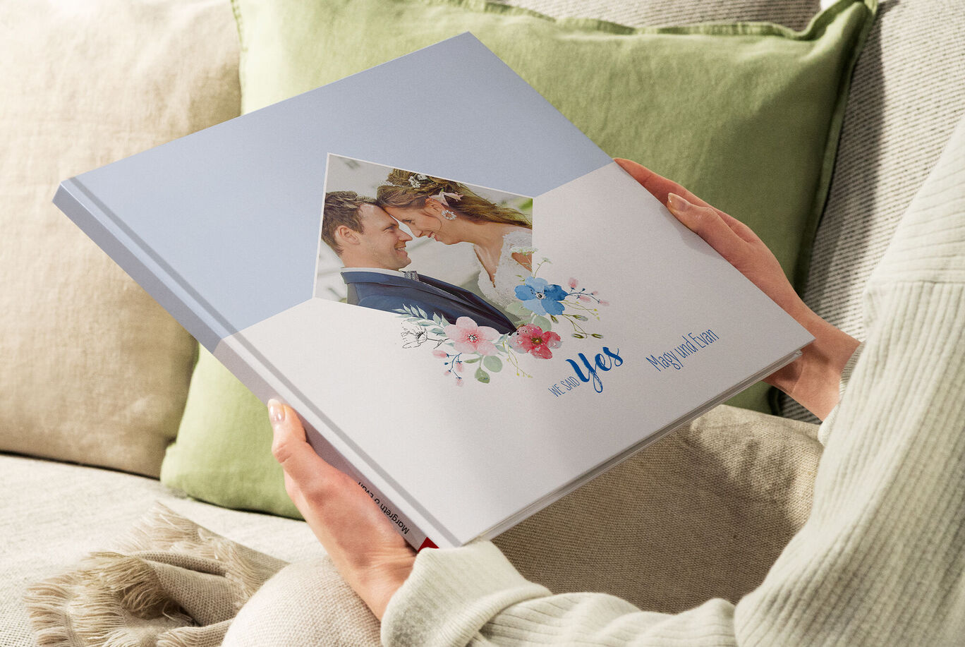 Eine Person hält ein CEWE Fotobuch mit einem romantischen Cover in den Händen. Das Cover zeigt florale Elemente und den Text 'Yes'.
