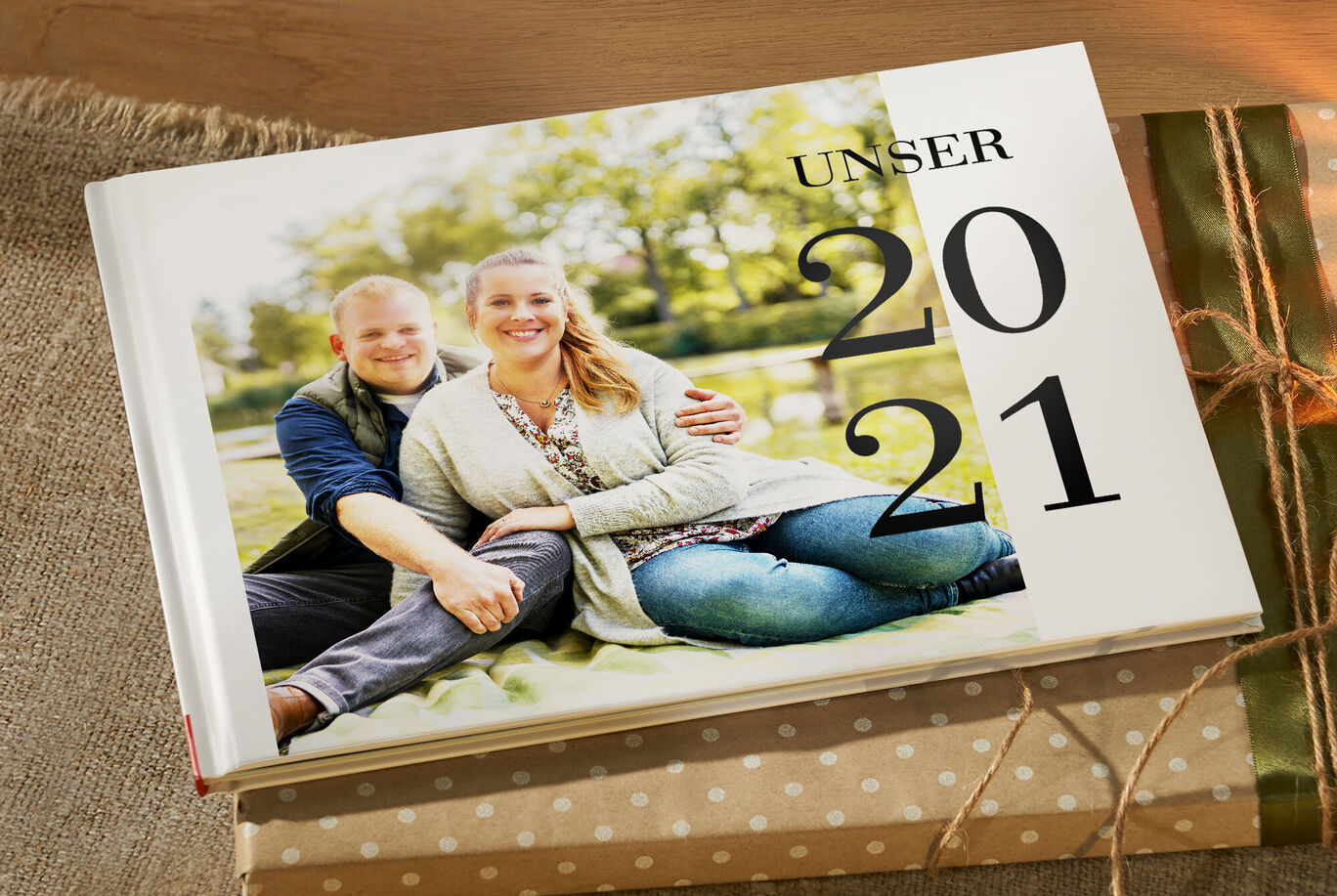 Ein CEWE FOTOBUCH 2021, das auf einem Tisch liegt, umgeben von Geschenken, mit einer fröhlichen Familie auf dem Cover