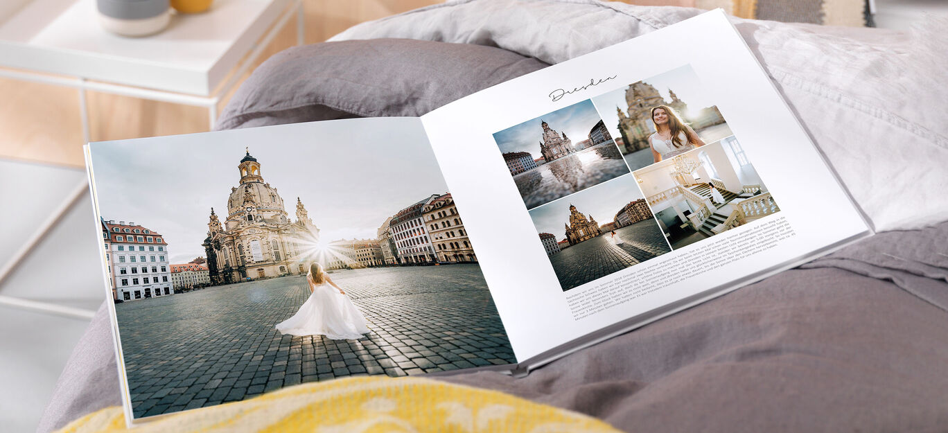 Eine Braut freut sich im Sonnenlicht auf einem Platz vor einer beeindruckenden Architektur. Sie hält ein neues Fotobuch in der Hand.