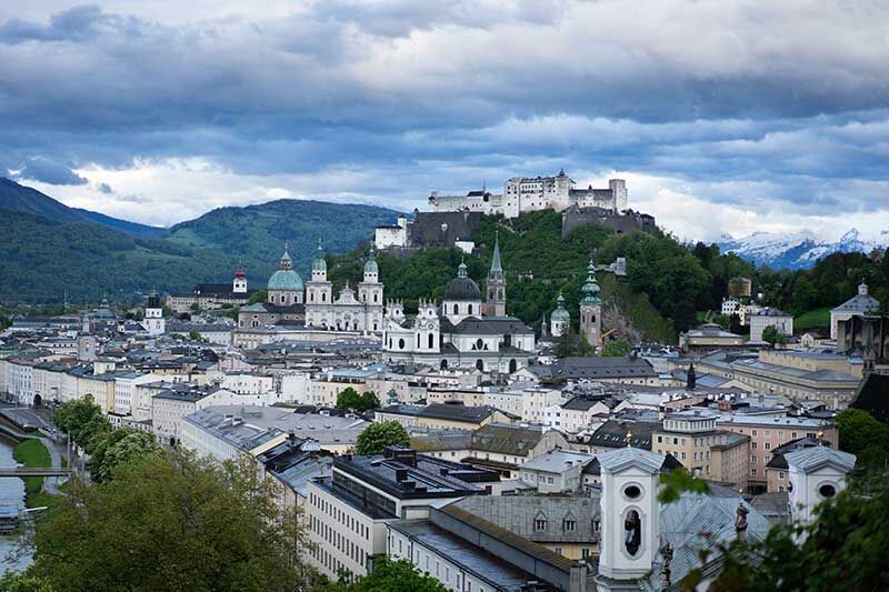 Blick über Salzburg mit der Festung Hohensalzburg im Hintergrund, umgeben von grünen Hügeln