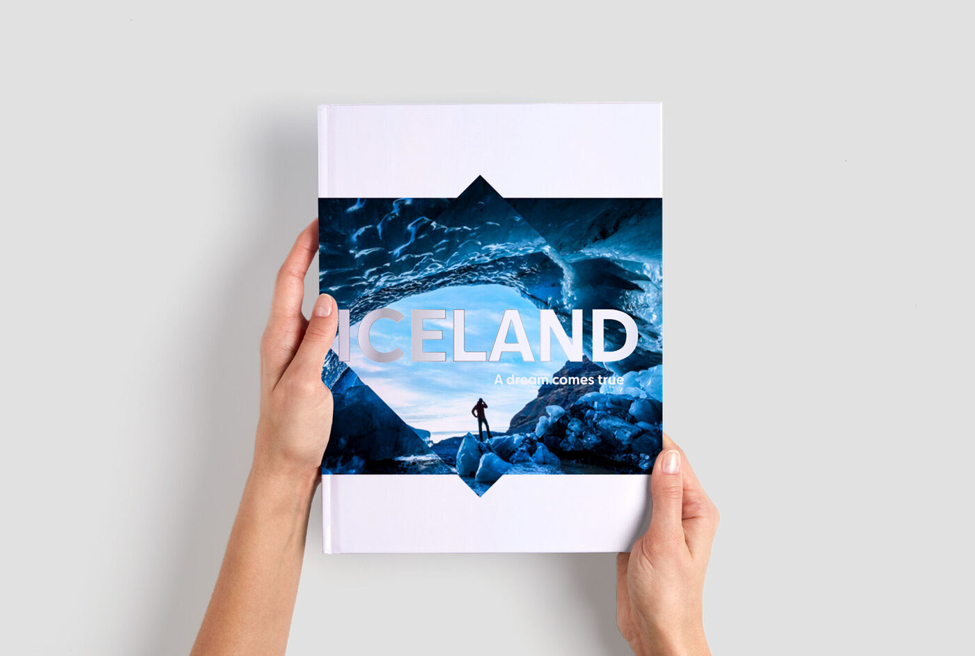 Eine Person hält ein CEWE FOTOBUCH mit dem Titel 'ICELAND' in den Händen. Das Buch zeigt eine beeindruckende Landschaft mit blauen Farbtönen.