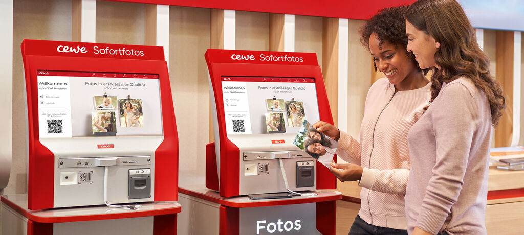 Zwei Personen am CEWE Sofortfoto-Automaten, beim Auswählen von Fotodrucken