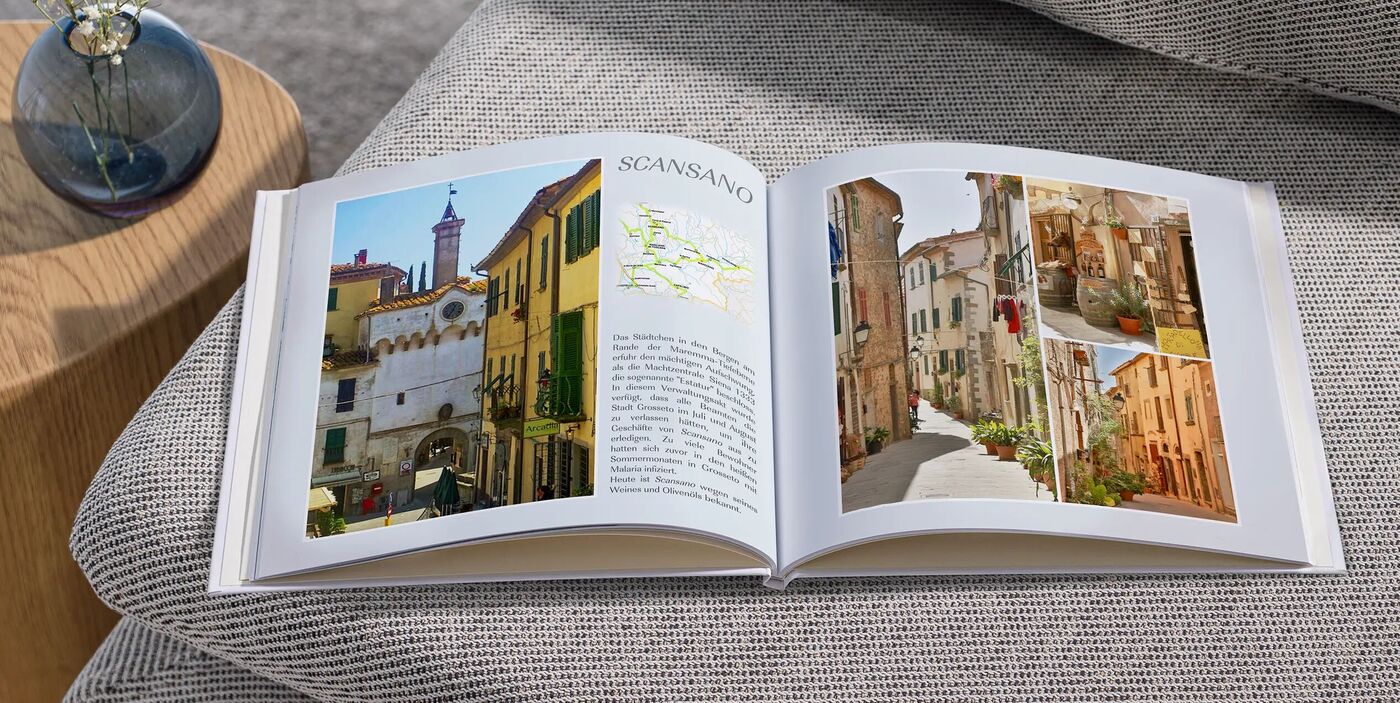 Aufgeschlagenes Fotobuch auf einem grauen Sofa; es sind Bilder einer italienischen Altstadt mit schmalen Gassen und bunten Häusern zu sehen.
