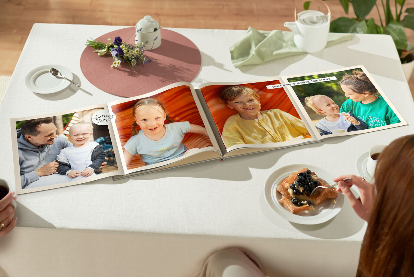 Ein offenes CEWE FOTOBUCH liegt auf einem Tisch neben einer Tasse Kaffee und einem Dessert. Es zeigt verschiedene Fotos von glücklichen Momenten mit Freunden oder Familie, die Freude und gemeinsames Erleben widerspiegeln